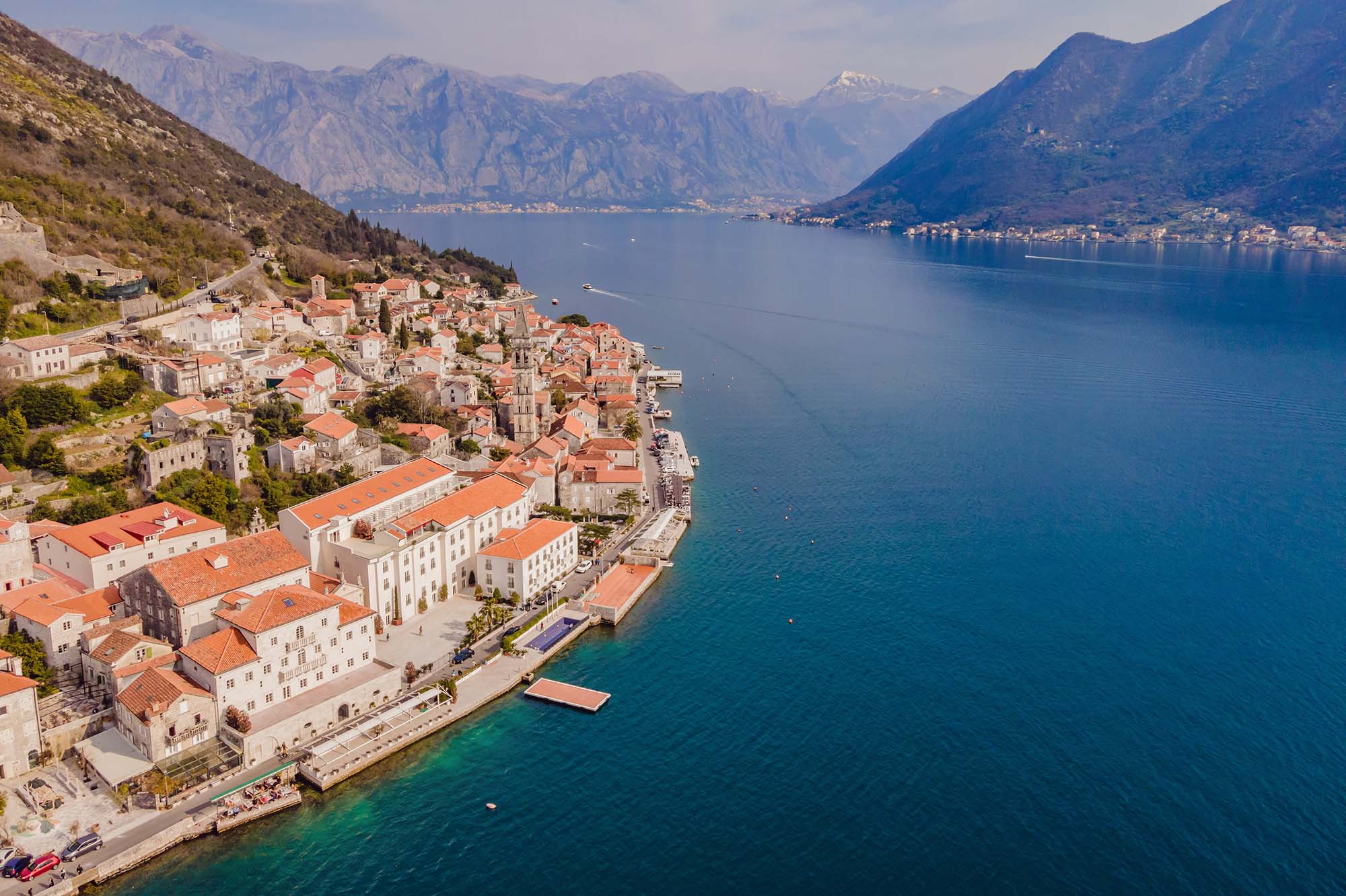Scenic panorama view of the historic town of Perast at famous Bay of Kotor with blooming flowers on a beautiful sunny day with blue sky and clouds in summer, Montenegro, southern Europe