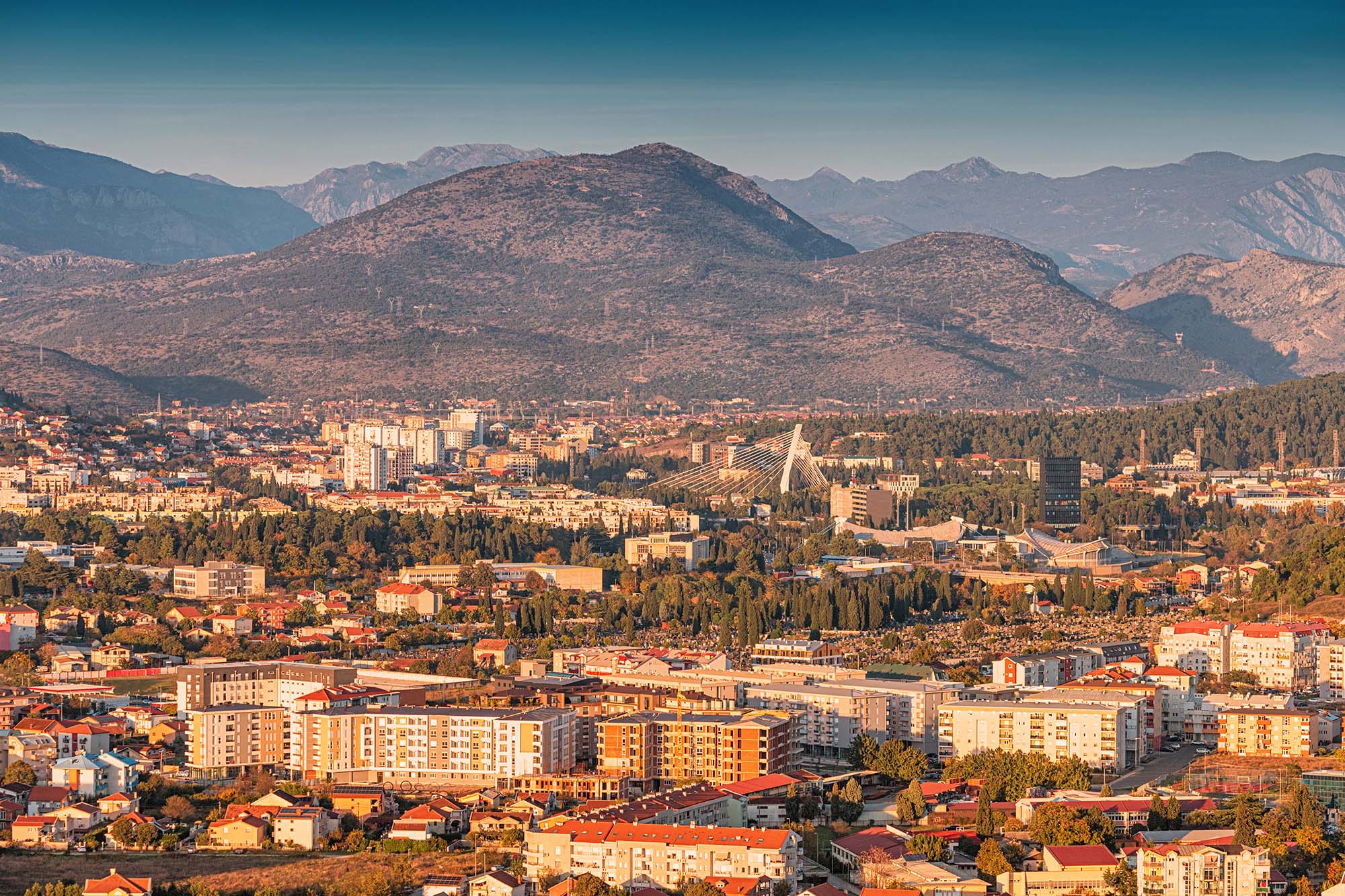 Modern cityscape panorama of Podgorica with bridge and surrounding mountains bathed in golden light